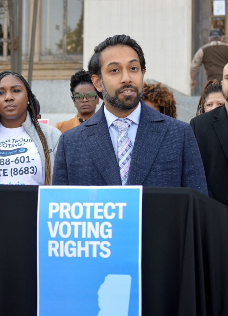 Amir Badat with NAACP Legal Defense Fund speaking at a rally with signs that say Protect Voting Rights