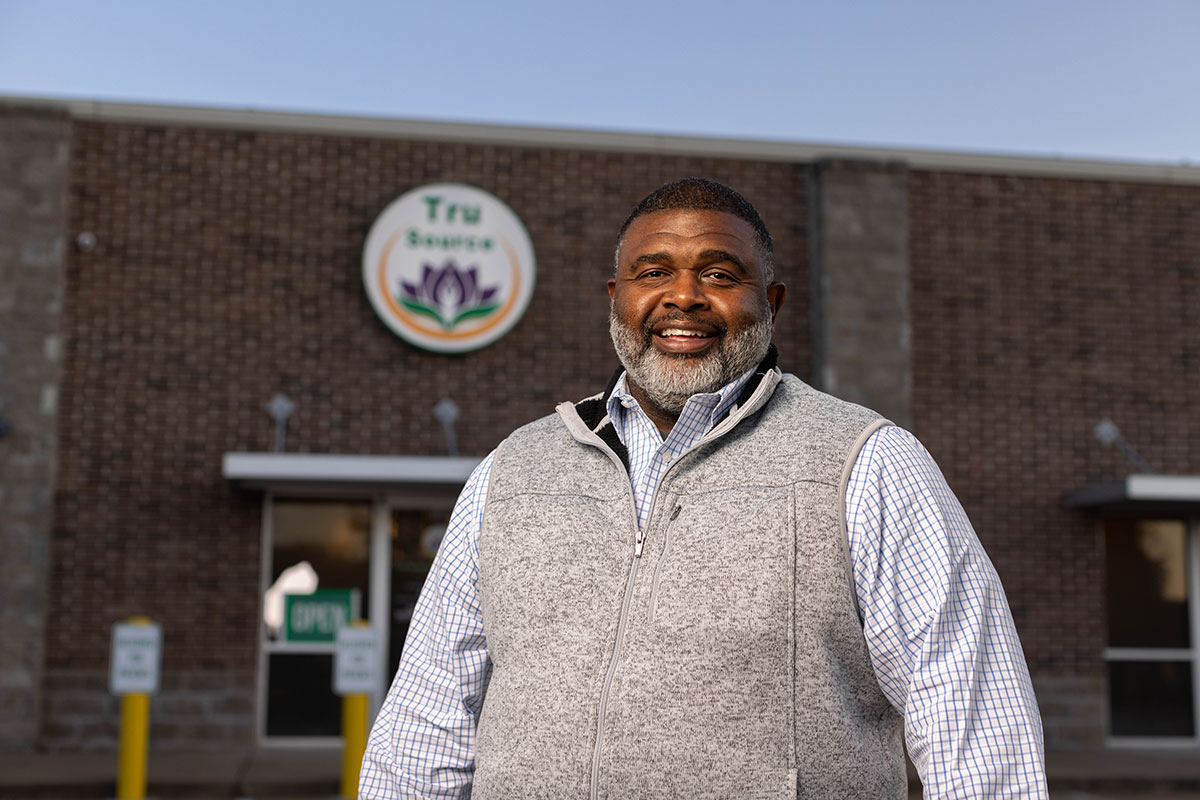 Clarence Cocroft stands outside of a business with a sign that reads Tru Source