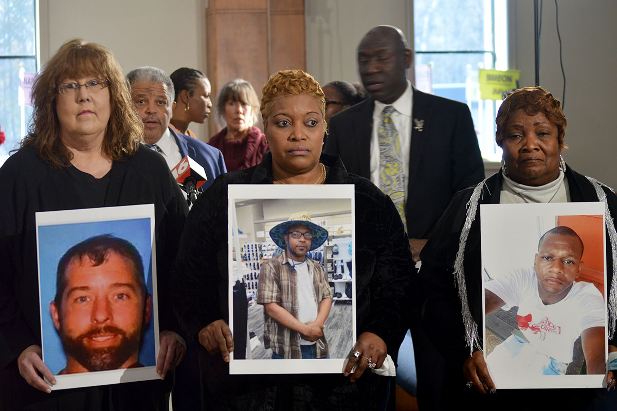 Three mothers hold up large poster photos of their sons at a press conference