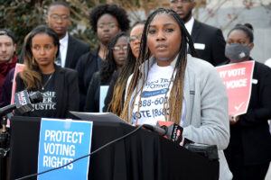 Kyra Roby with One Voice Mississippi speaking at a rally with signs that say Protect Voting Rights