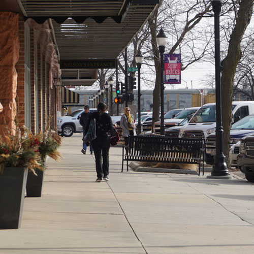 A small number of people walk down a downtown sidewalk in front of businesses