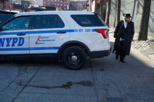 A Hasidic man walks past a police patrol car i