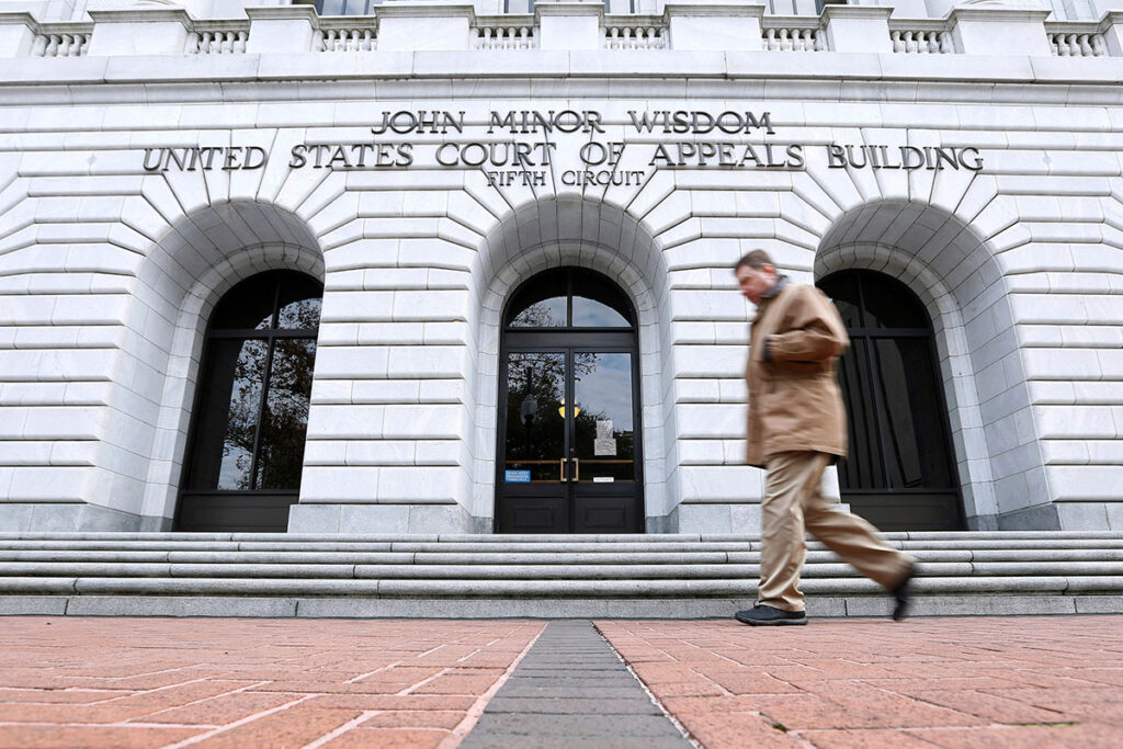 A man walks past a building labeled "John Minor Wisdom, United States Court of Appeals Building, Fifth Circuit"