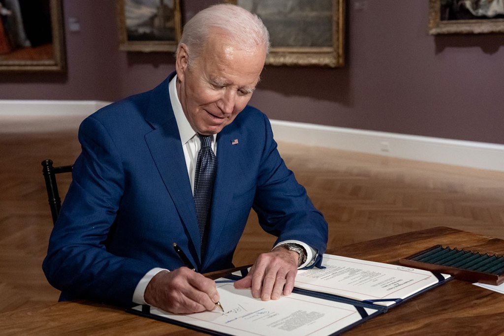 President Joe Biden signs something on a desk