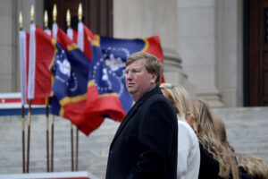 Gov. Tate Reeves walks with his family past MS state flags