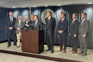 eight men standing around a podium; gov. Tate Reeves is standing at the podium with Delbert Hosemann and jason white next to him