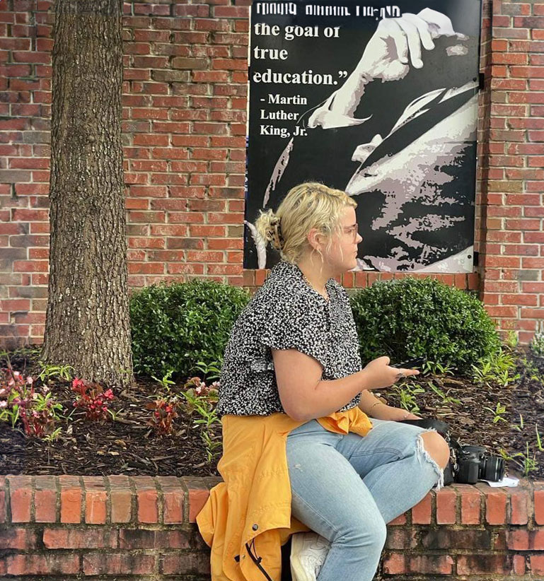 Heather Harrison sitting on a brick wall and recording an interview