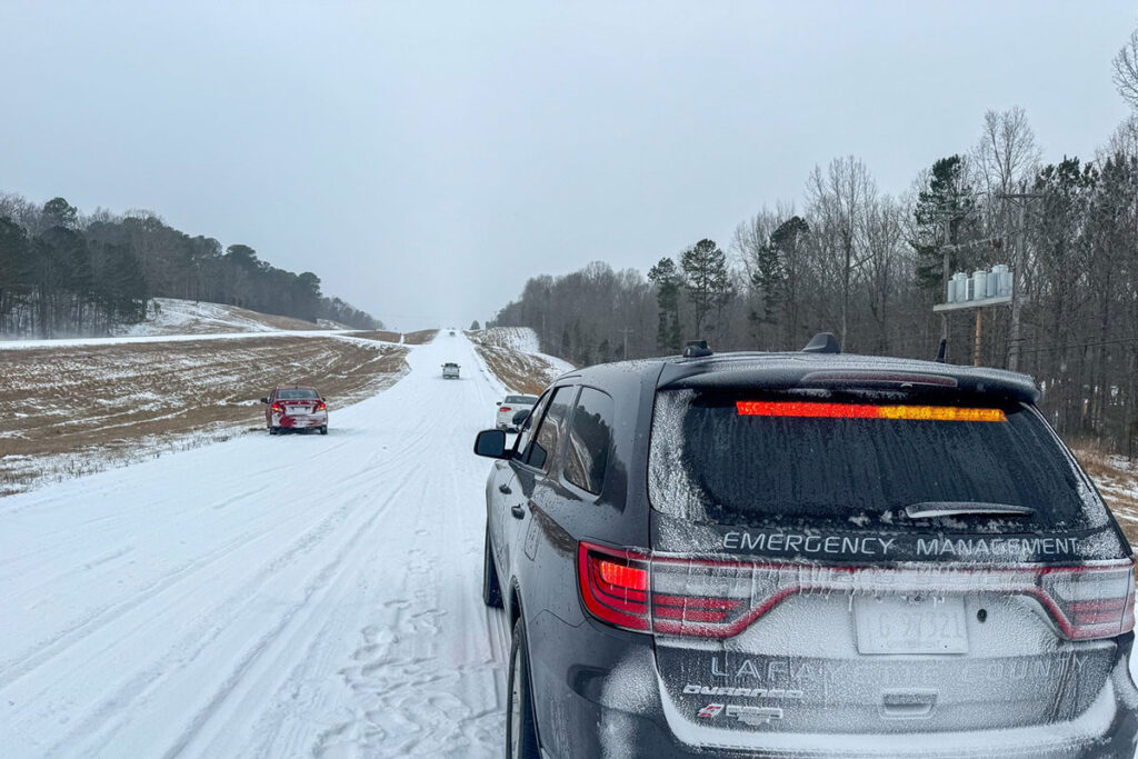 An Emergency vehicle drives slowly down a snowy highway, cars visibly off on the side