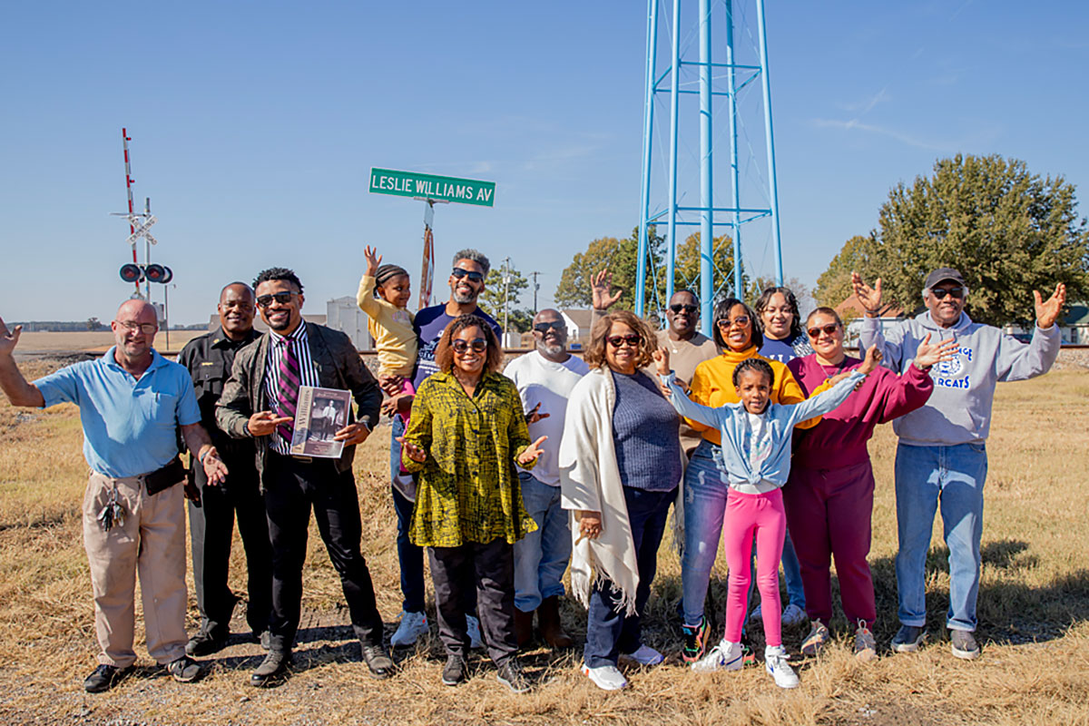 A family standing by a street sign that reads "Leslie Williams AV"