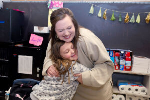 A young student hugs her teacher