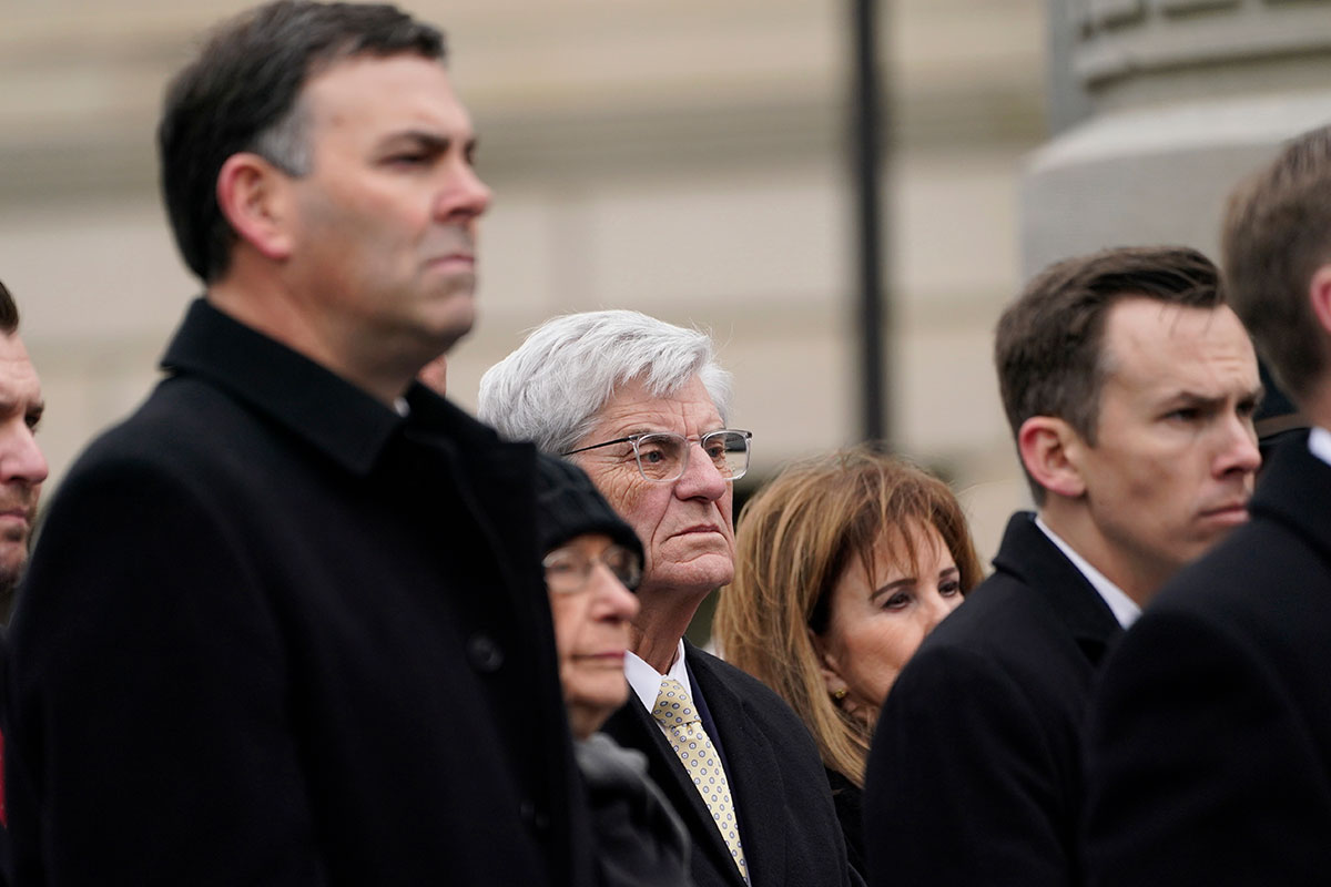 three men stand in a crowd listening
