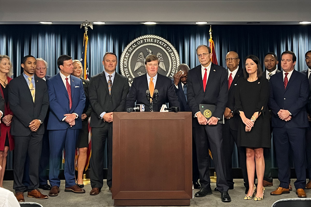 Lawmakers stand behind a podium. The great seal of the state of Mississippi is behind them.