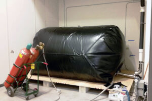 A large black inflated bag sits on a small raised platform with two red air tanks attached by a hose