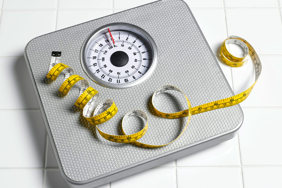 Tape measure lying on top of a scale on a white tile background (obesity-fighting drug)