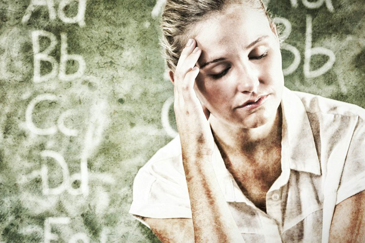 A woman in front of a chalkboard holds her head as though with a headache