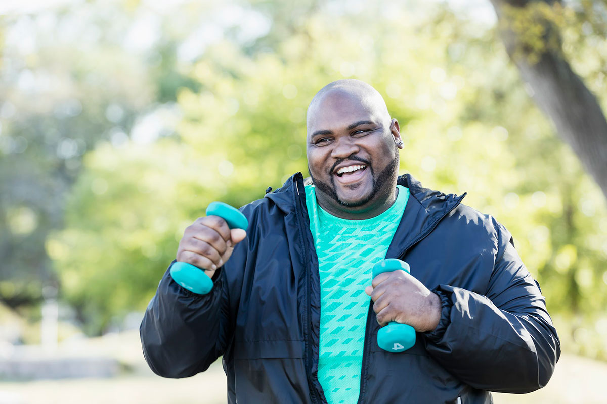smiling man outside in jacket with small hand weights (health goals)
