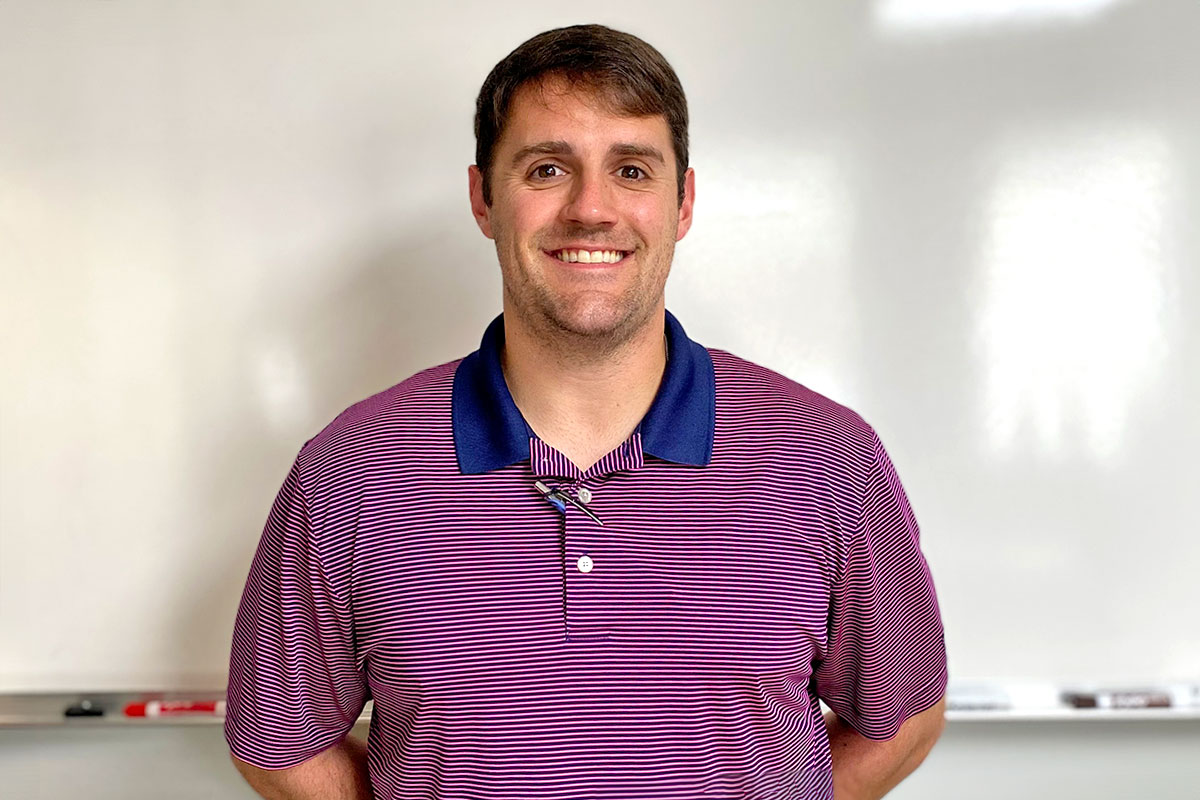 A man in a red top stands in front of a whiteboard inside a classroom