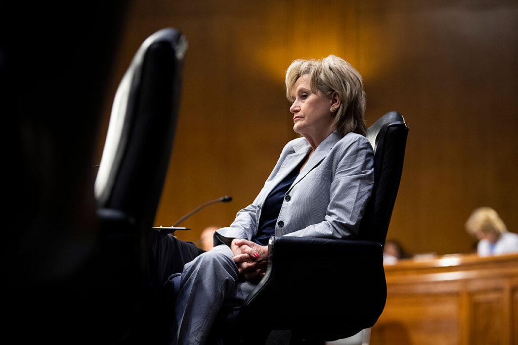 A woman reclining in a large dark seat in the senate chambers