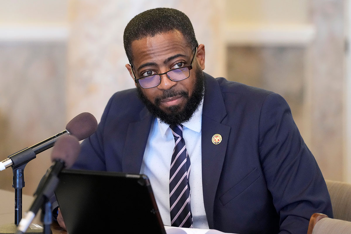 Fabian Nelson, in a navy suit, speaks at a legislative committee meeting
