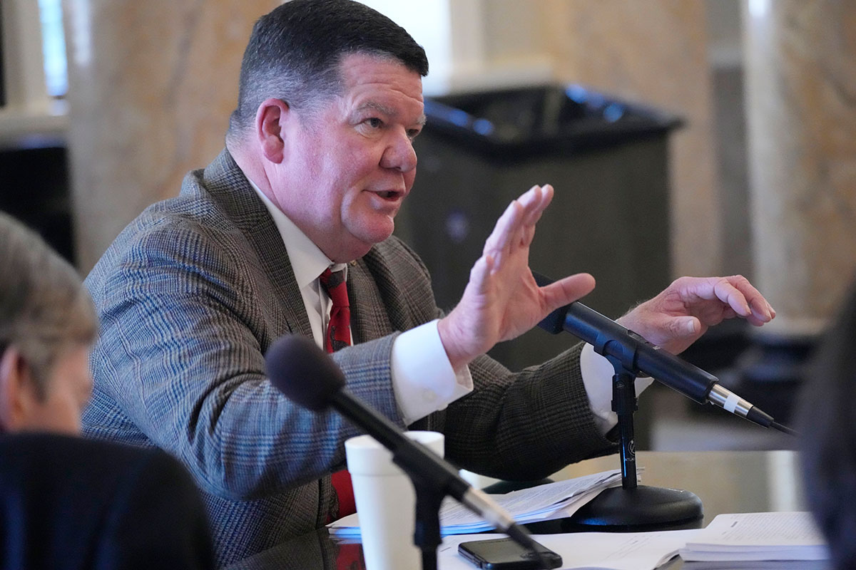 Sam Creekmore, IV, R-New Albany, speaks with committee members at a table covered in mics