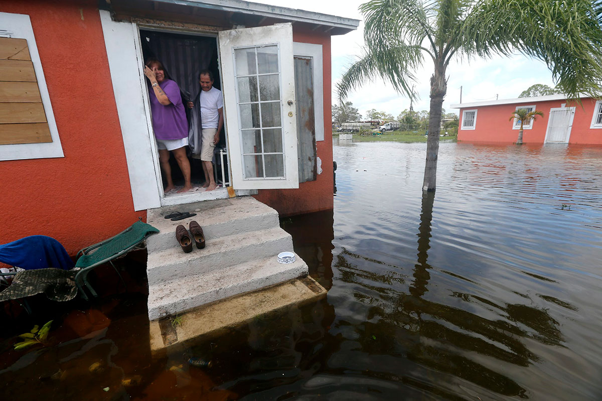 Two people look outside their front door as water floods into the neighborhood