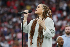 A woman with long twisted hair sings before a large audience at a Super Bowl game