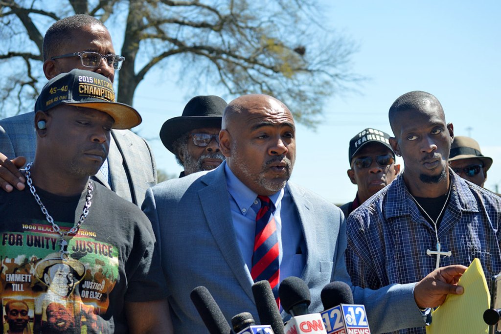 Several men stand outside to speak in front of local media microphones.