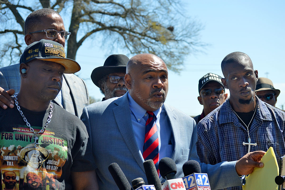 Several men stand outside to speak in front of local media microphones.