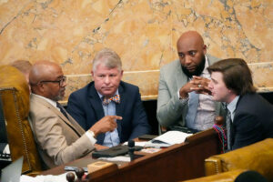 Four legislators lean forward and discuss inside the capitol