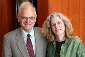 An older man in a light grey suit poses beside a woman in a green top