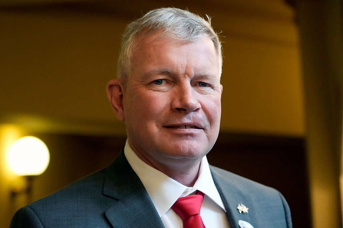 Close up of a older man with greying hair and wearing a grey suit and red tie