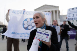 A person holds a box of mifepristone tablets in one hand and a megaphone in the other at an abortion rights rally