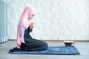 A young Muslim student in pink headscarf prays on a blue rug