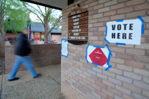 A man walks through a brick building with "Vote Here" signs taped to the wall