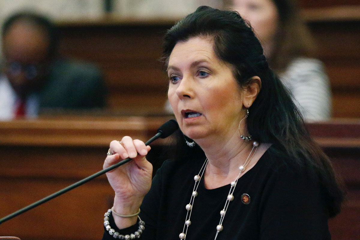 A woman in black clothes speaks at a mic in the senate