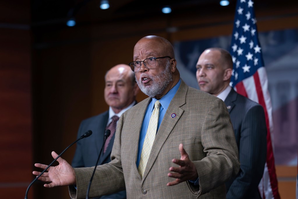 Bennie Thompson speaks at a podium with arms held out in question. Two other men stand behind him.