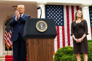 President Donald J. Trump stands on the left side of the image while Judge Amy Coney Barrett is on the right, separated by a presidential podium.