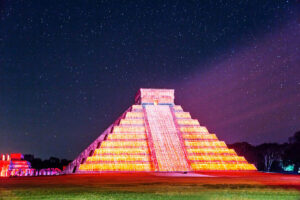 A Mayan pyramid light up before a starry night sky