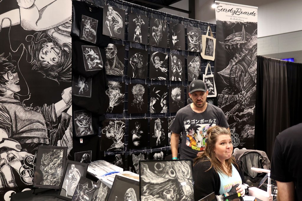 An artist sits at a booth filled with white linework ark on black backgrounds