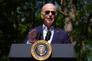 President Joe Biden speaks at an official podium while wearing sunglasses