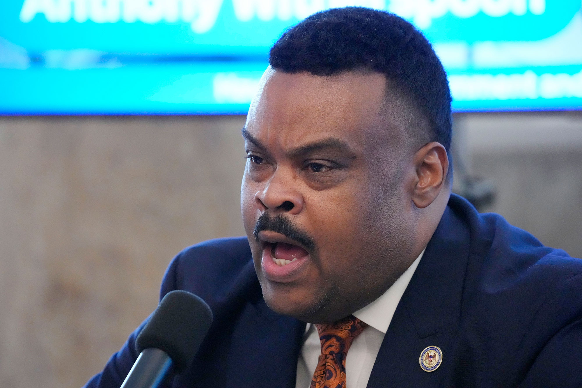 A man in a blue suit speaks into a mic