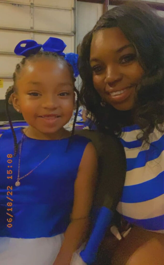 A woman and her younger daughter pose together in matching blue outfits