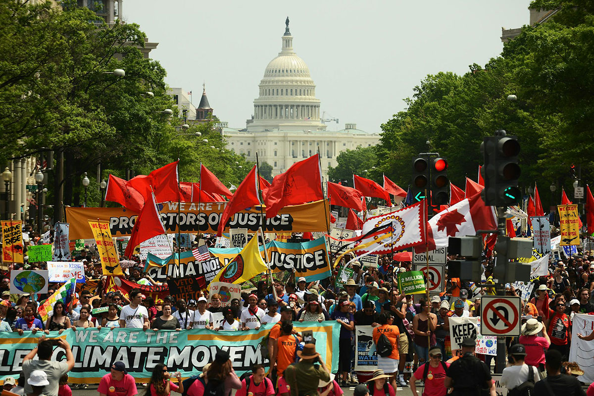 A large crowd of people march and wave banners and red flags in front of the US Capitol building (climate change)