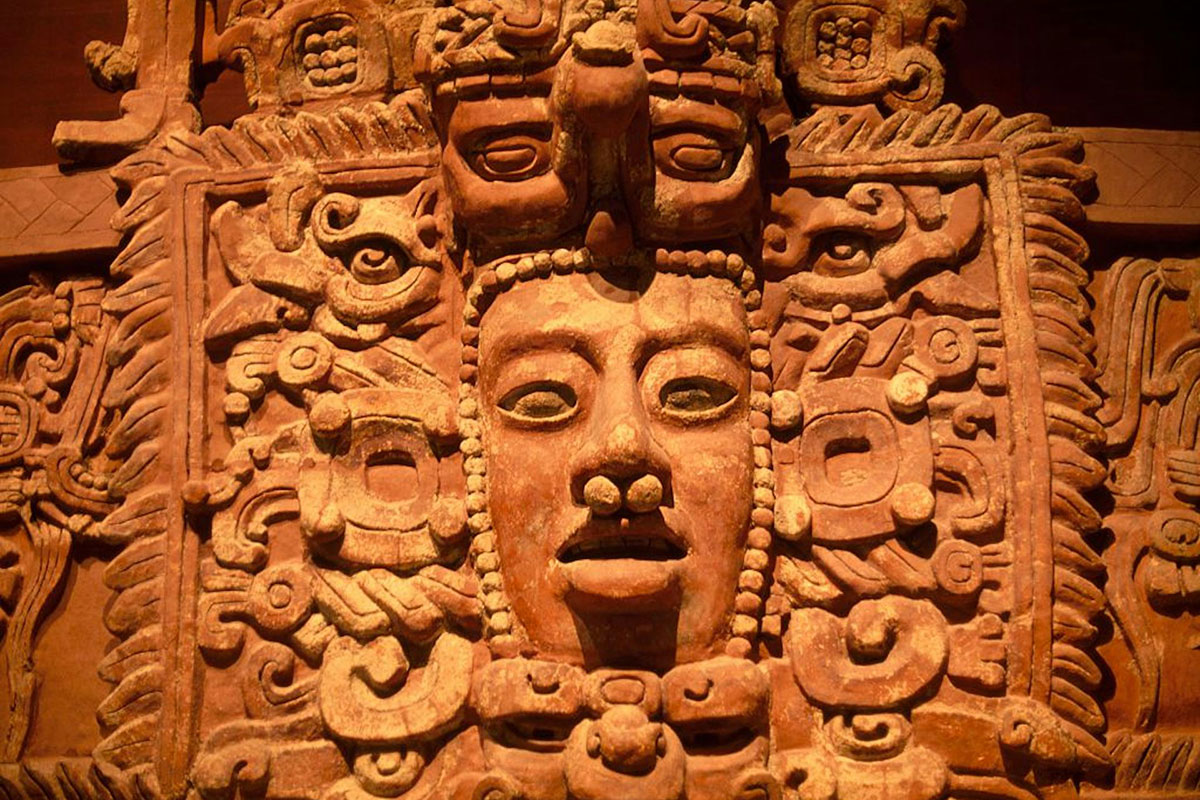 "A large clay-colored decoration with intricate carvings and a face with eyes, a pierced nose and a mouth