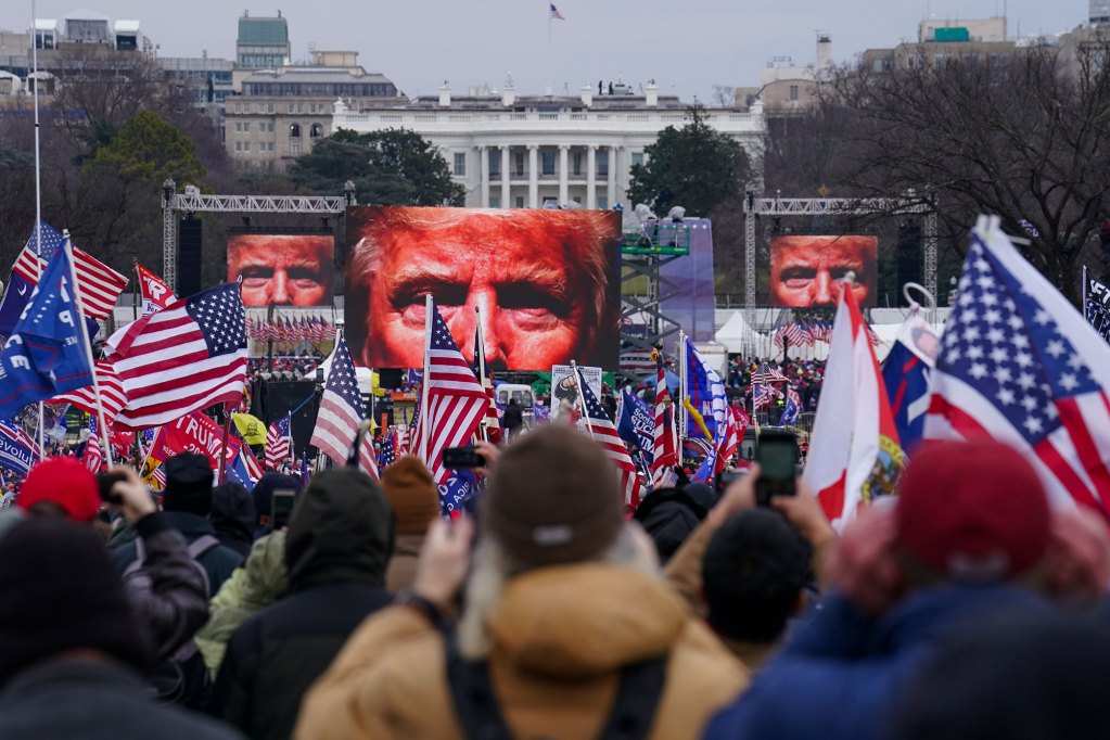 A crowd of people holding small US Flags in the air assemble in before giant posters of Donald Trump's eyes