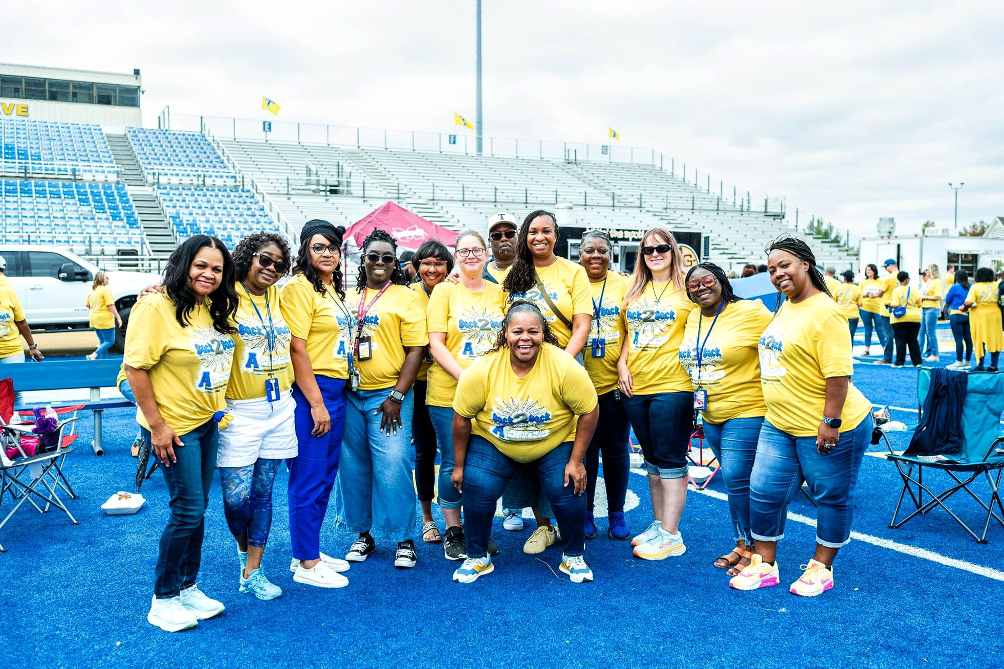 A row of people in matching yellow shirts pose outside on a blue colored football field
