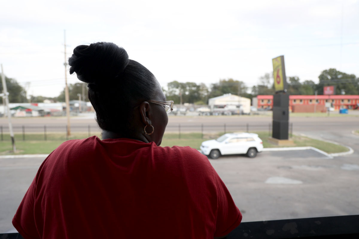 The back view of a woman in a red top and a yellow sign with a visible 6 in the distance
