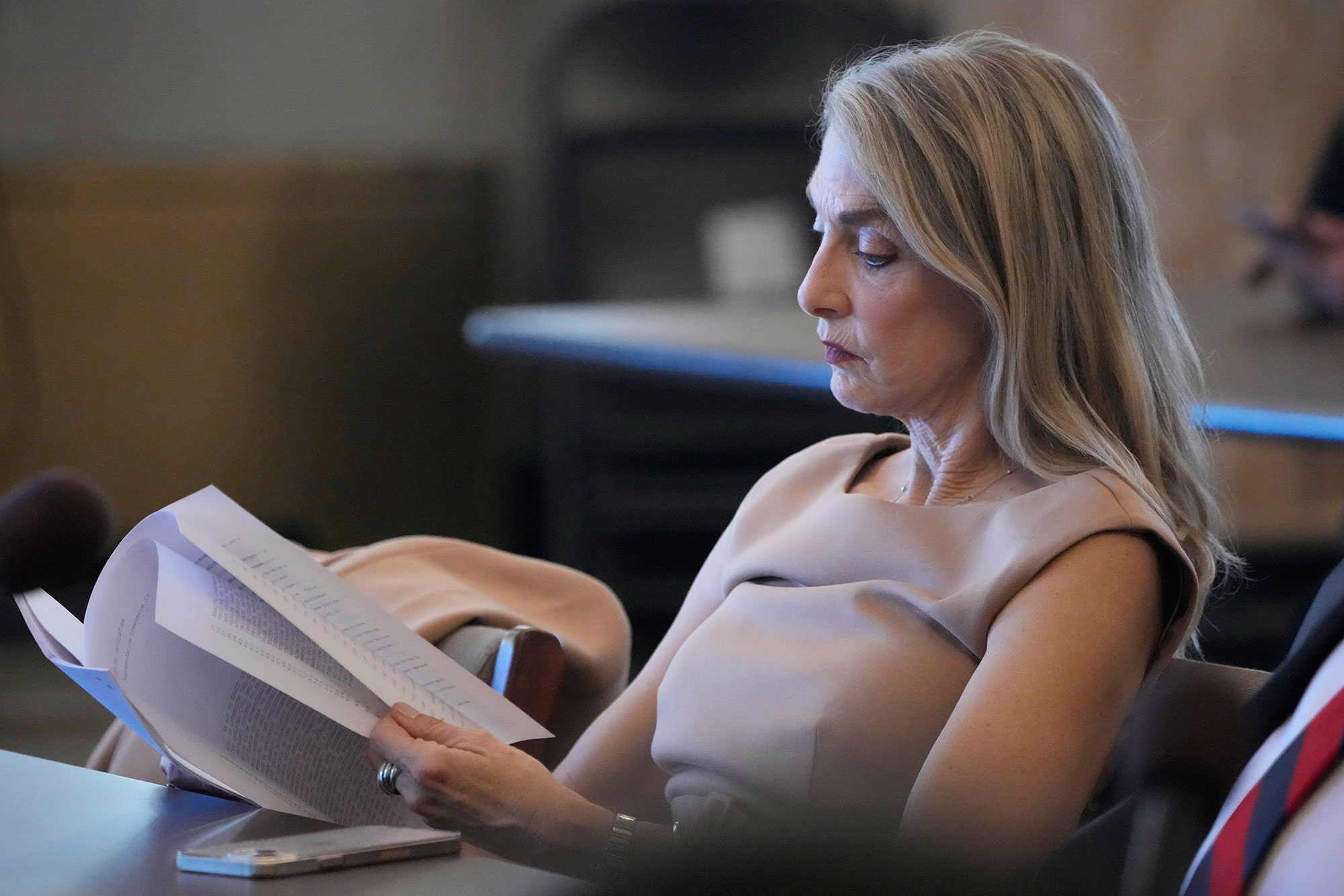 A woman sits at at table and reads through a stack of papers