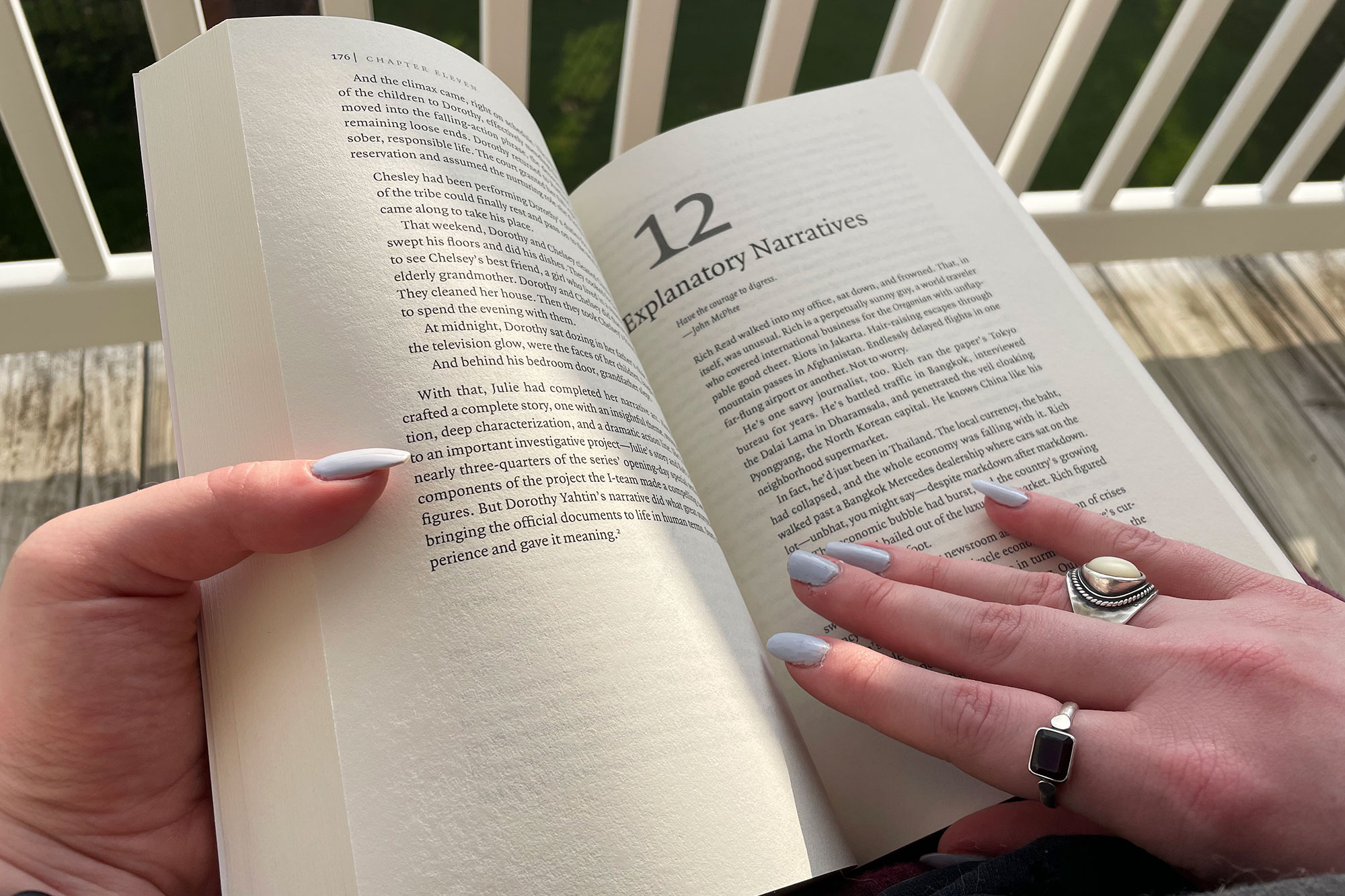 A be-ringed hand holds a book open to a page labeled 12: Explanatory Narratives