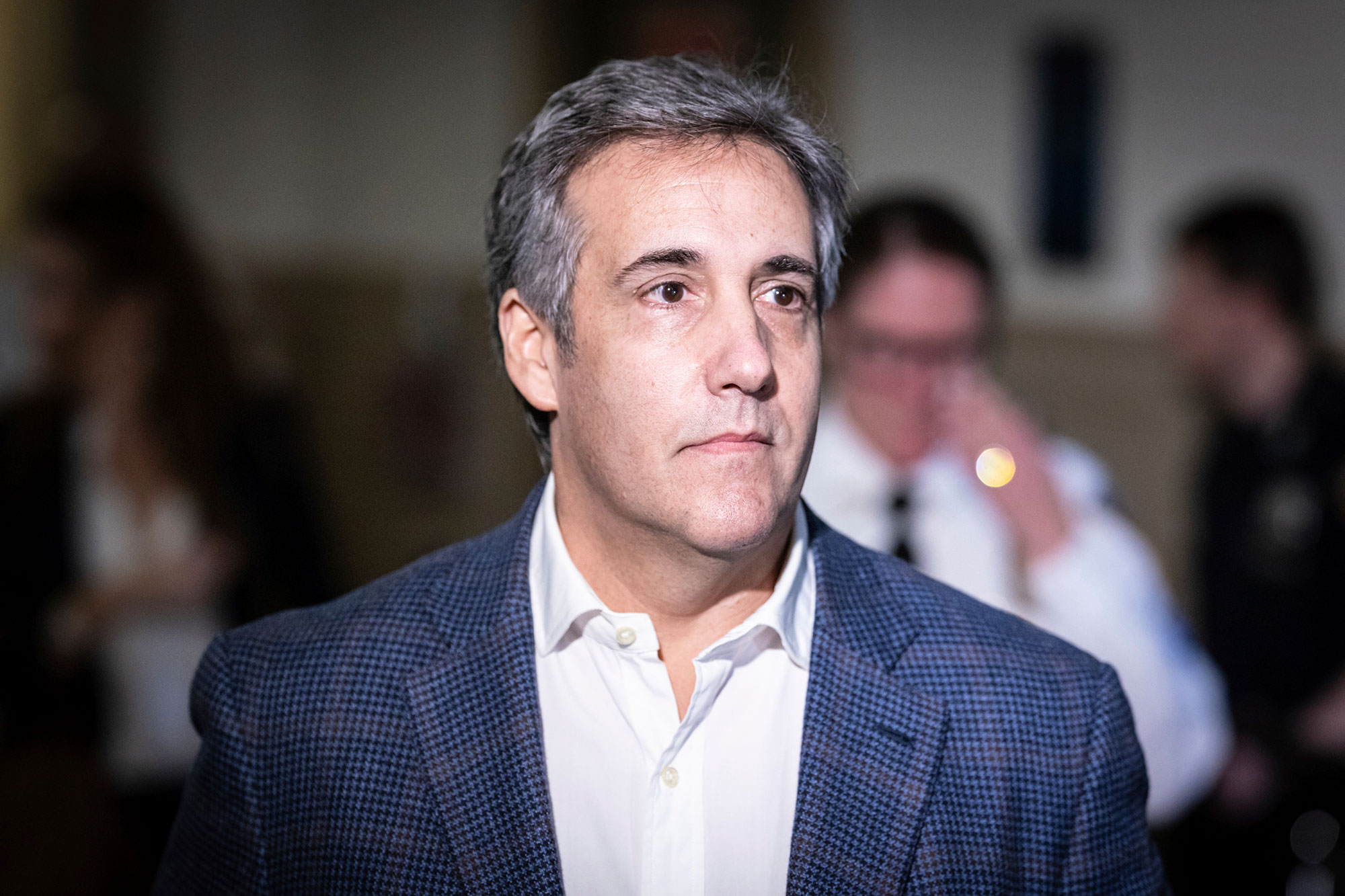 A man in a lightly checkered blue suit button-down shirt with no tie looks off in the right distance